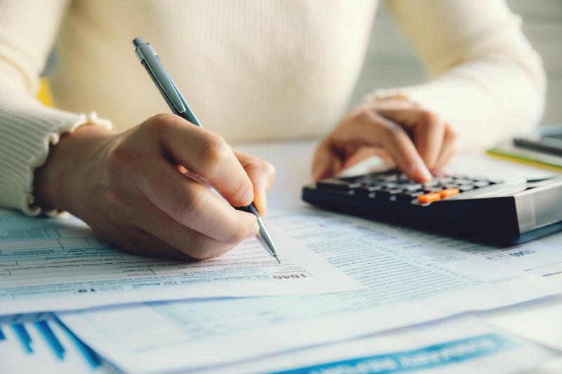 A close up of hands, one writing on a piece of paper and another punching numbers in on a calculator
